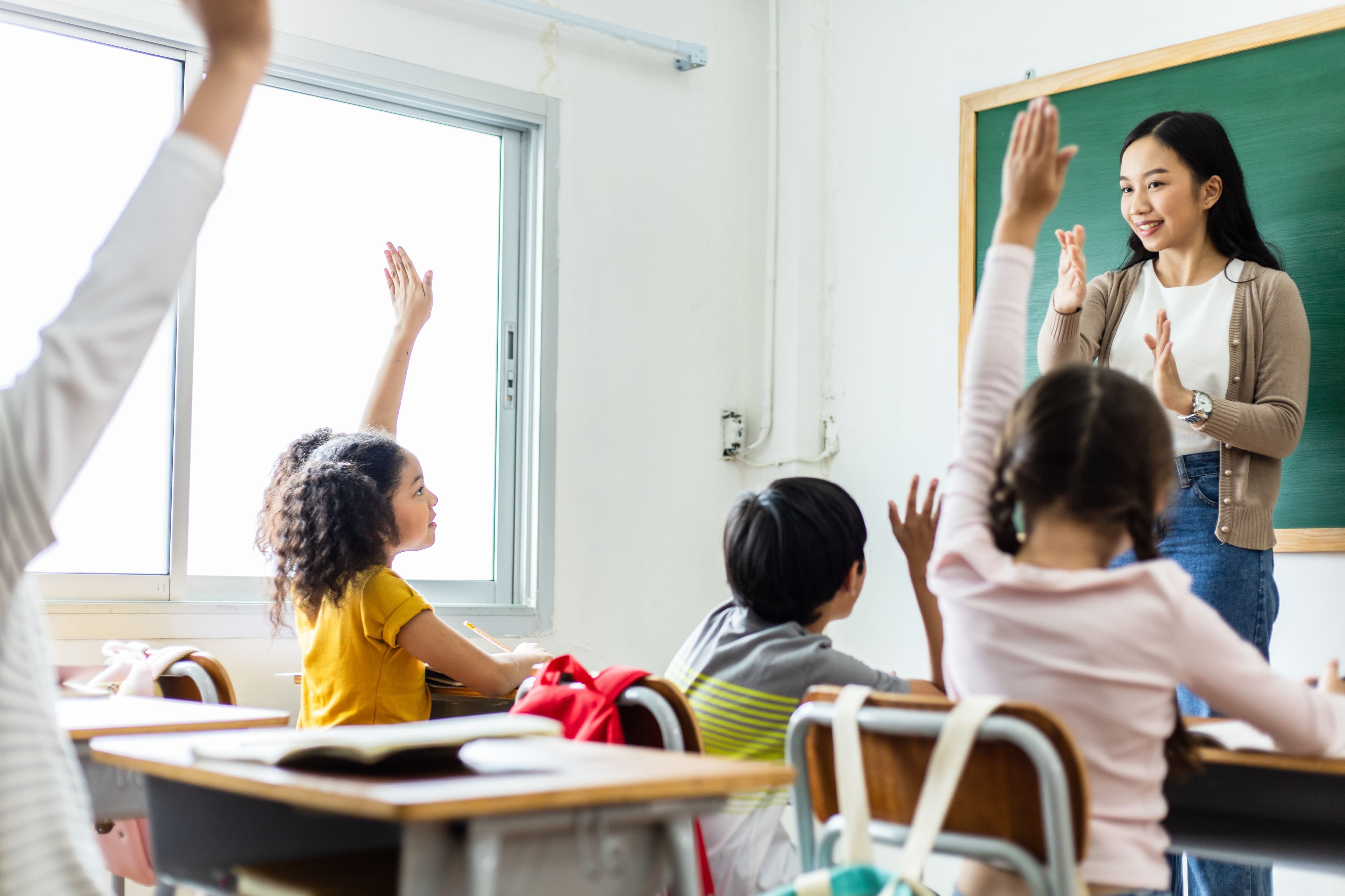 Female teacher and children with raised hands